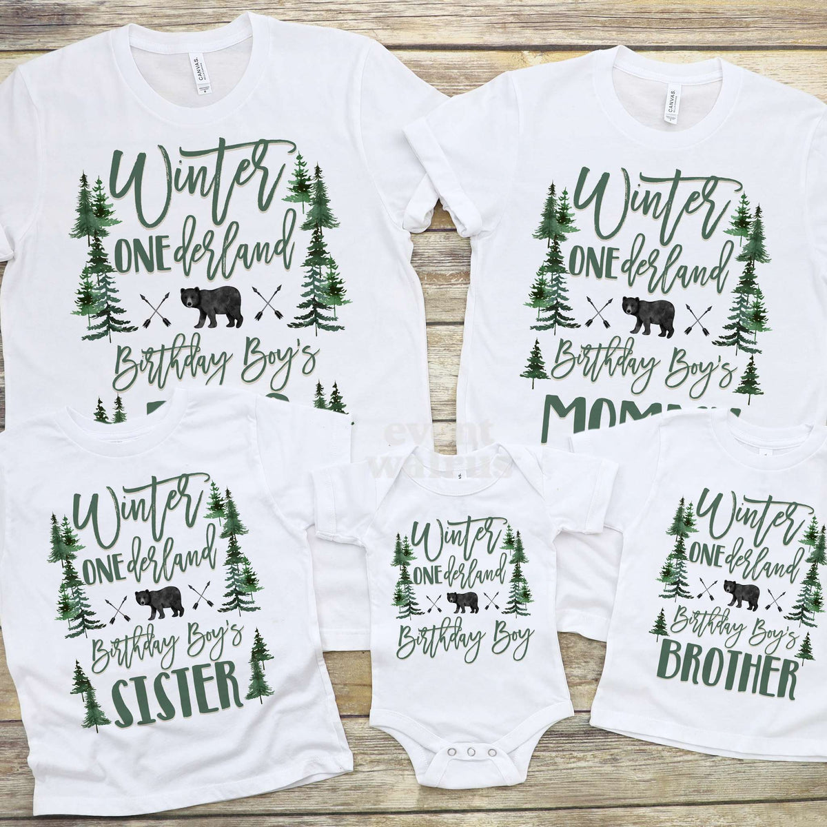 Bear forest Winter ONEderland family shirts and a Birthday Boy bodysuit with green pines, laid out on wood