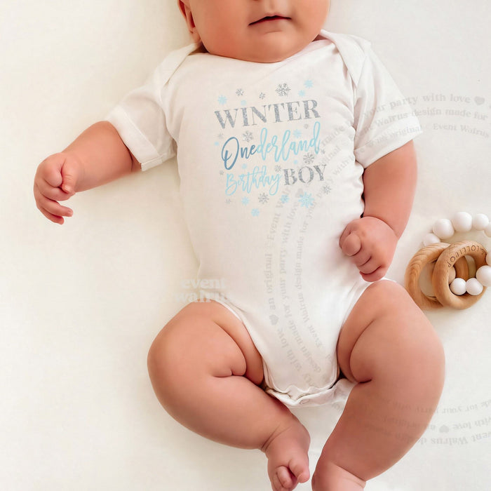 Baby lying on a white blanket in a blue and silver Winter Onederland Birthday Boy bodysuit.