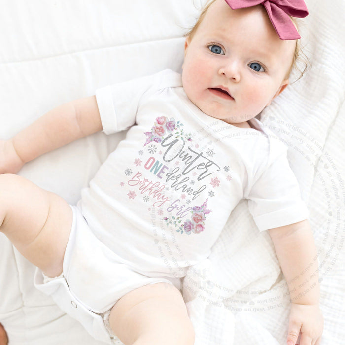 Baby girl with a pink bow lying in a white floral Winter ONEderland Birthday Girl bodysuit.