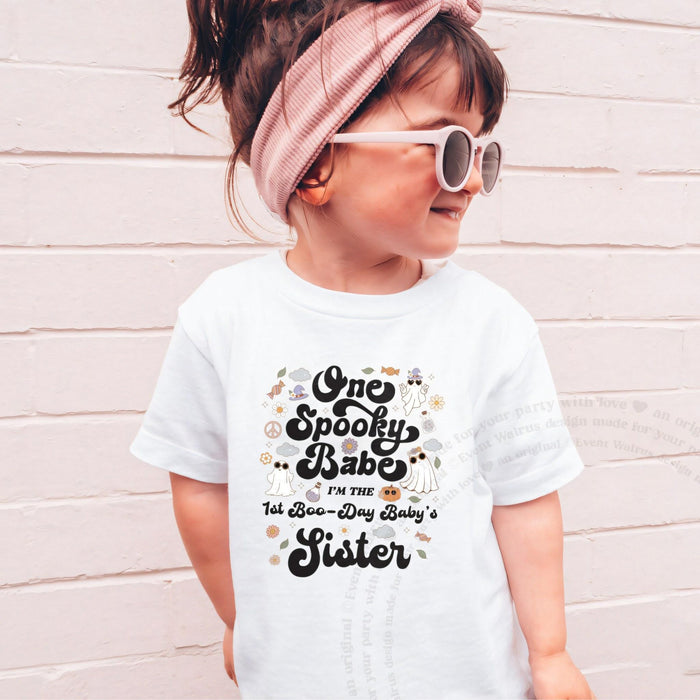 Girl in sunglasses and a pink headband wearing a white One Spooky Babe Sister shirt.