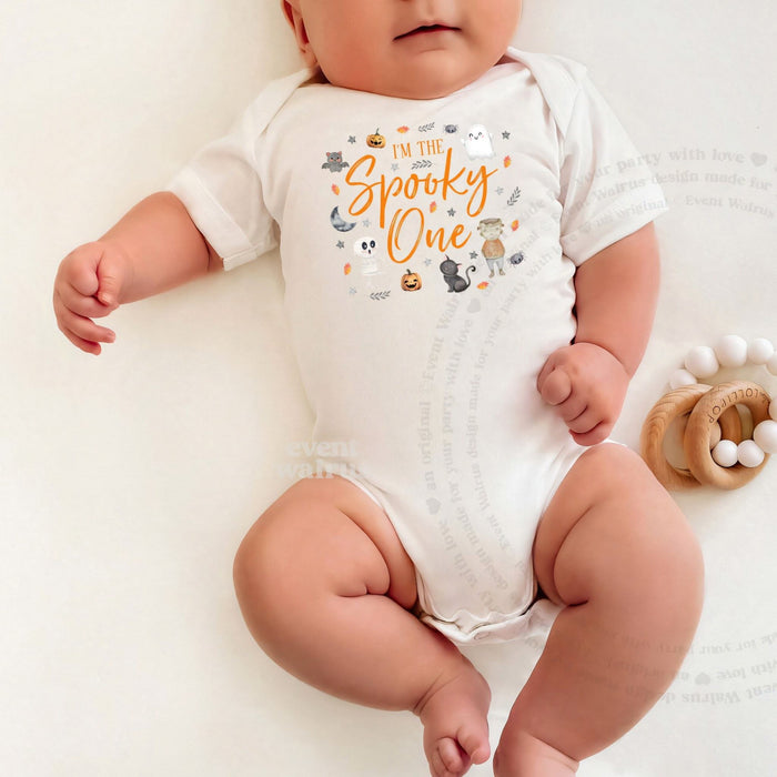 Baby lying on a white blanket in an I'm the Spooky One bodysuit with orange script.