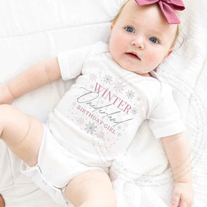 Baby girl with a pink bow lying in a white Winter Onederland Birthday Girl bodysuit.