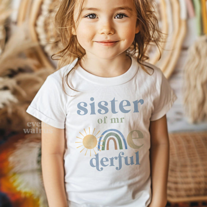 Smiling girl in front of a boho rainbow in a white Sister of Mr Onederful shirt.