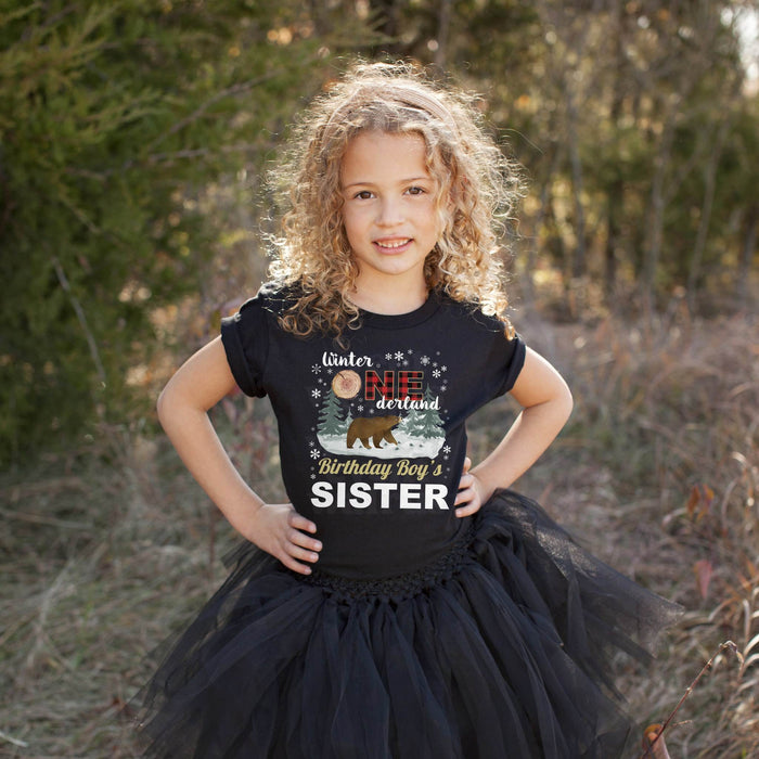 Girl in a tutu wearing a black Winter Onederland Birthday Boy's Sister shirt outdoors.