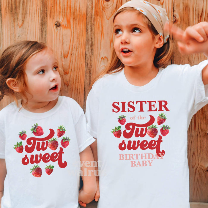 Two girls against a wood wall in white strawberry Two Sweet and Sister shirts.