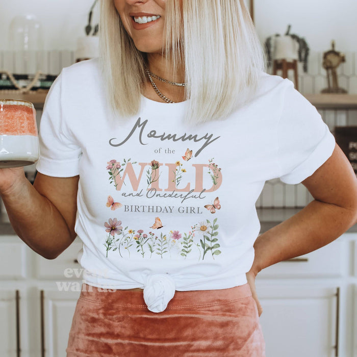 Mom holding a mug in a white Mommy of the Wild and Onederful Birthday Girl shirt with dusty pink wildflowers.