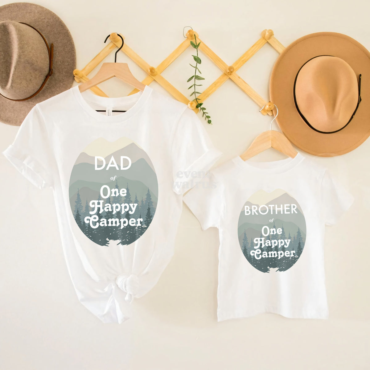 White Dad and Brother One Happy Camper tees with misty green mountains, hanging on a peg rail