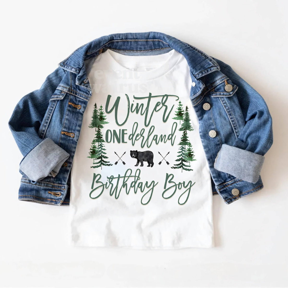 White Winter ONEderland Birthday Boy toddler tee laid on a denim jacket.