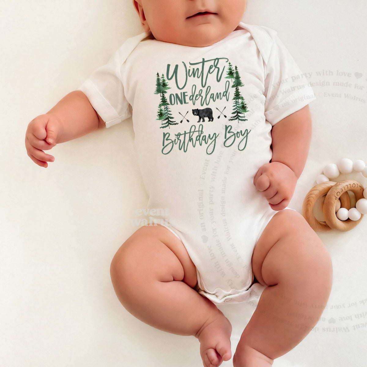 Baby lying on a white blanket in a Winter ONEderland Birthday Boy bodysuit with the black bear.