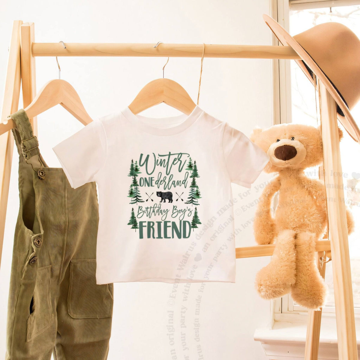 White bear forest Friend toddler tee on a wooden clothes rack beside a teddy bear.