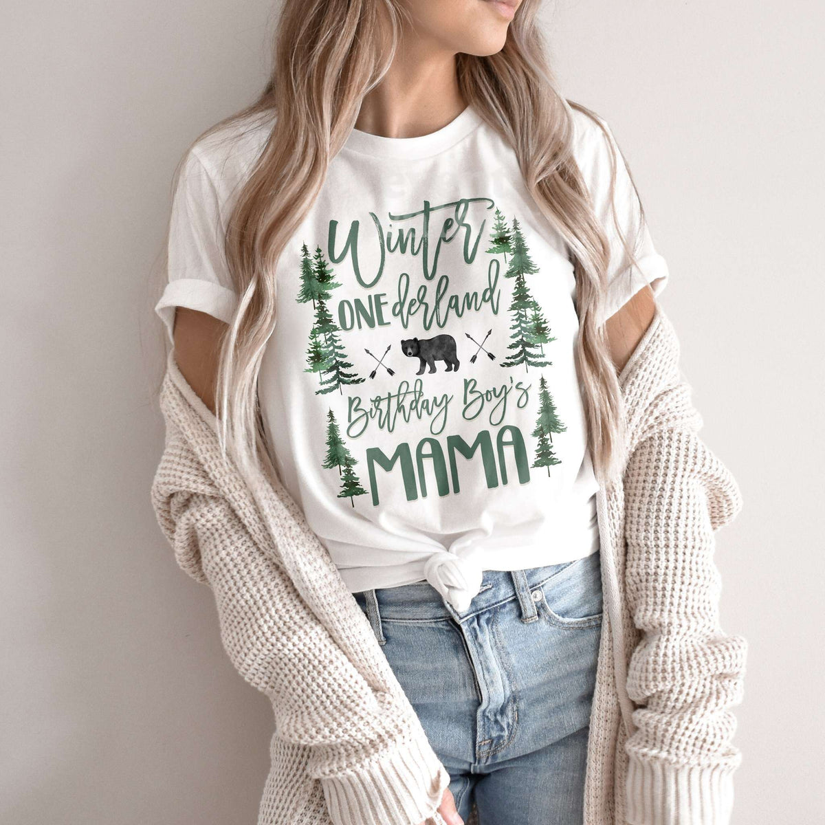 Woman in a knit cardigan wearing a white Winter ONEderland Birthday Boy's Mama shirt.