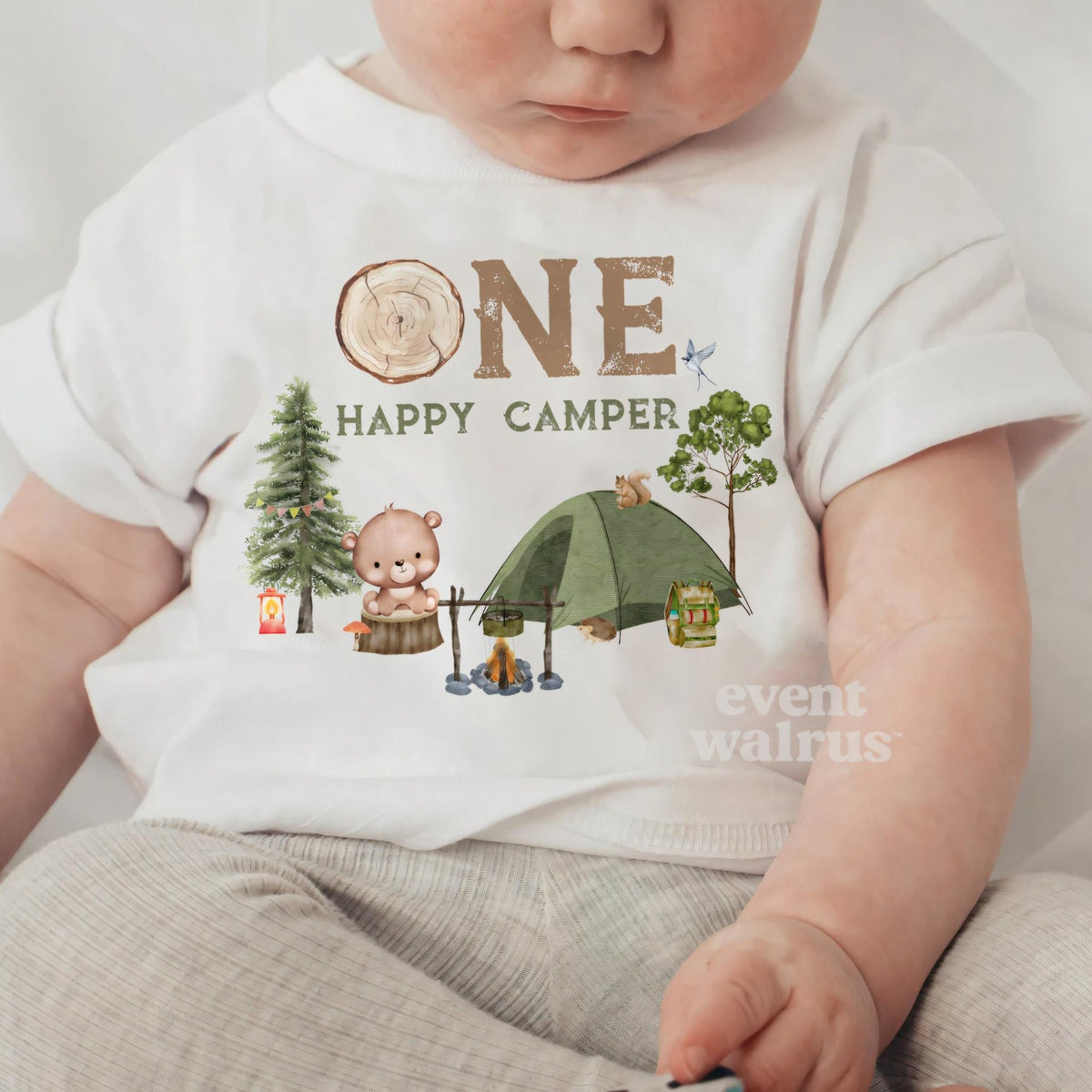 Baby sitting up in a white One Happy Camper baby tee.