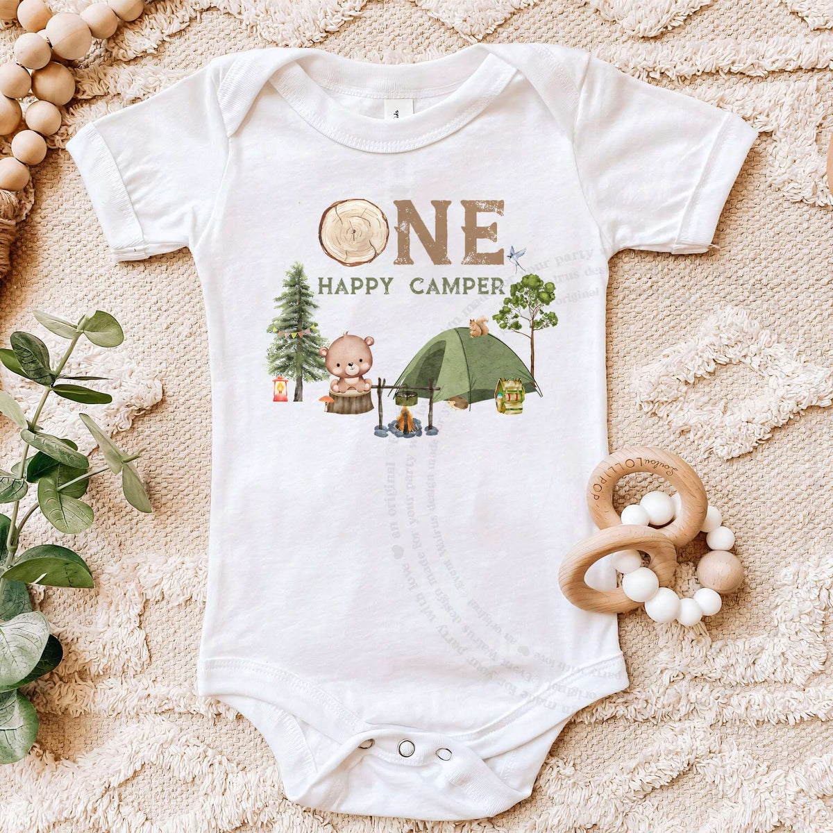White One Happy Camper bodysuit on a beige blanket with a wooden teether.