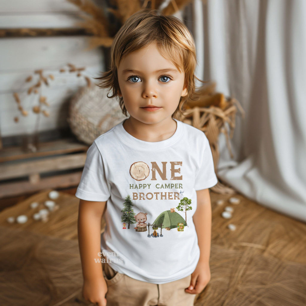 Little boy in a boho room wearing a white One Happy Camper Brother tee.