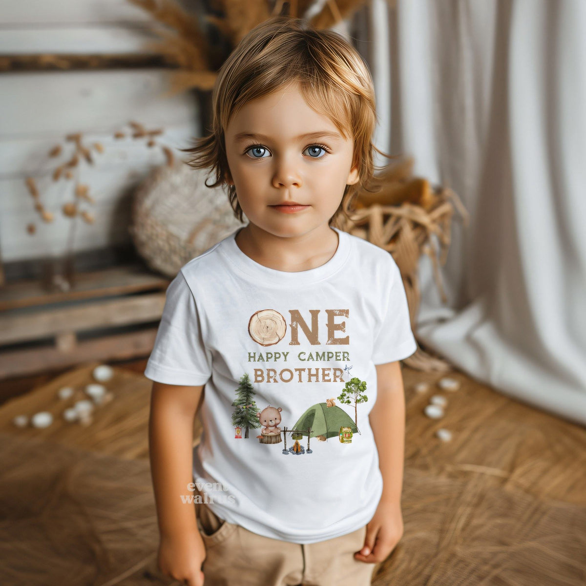 Little boy in a boho room wearing a white One Happy Camper Brother tee.