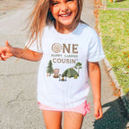 Laughing girl outdoors in a white One Happy Camper Cousin kids tee.