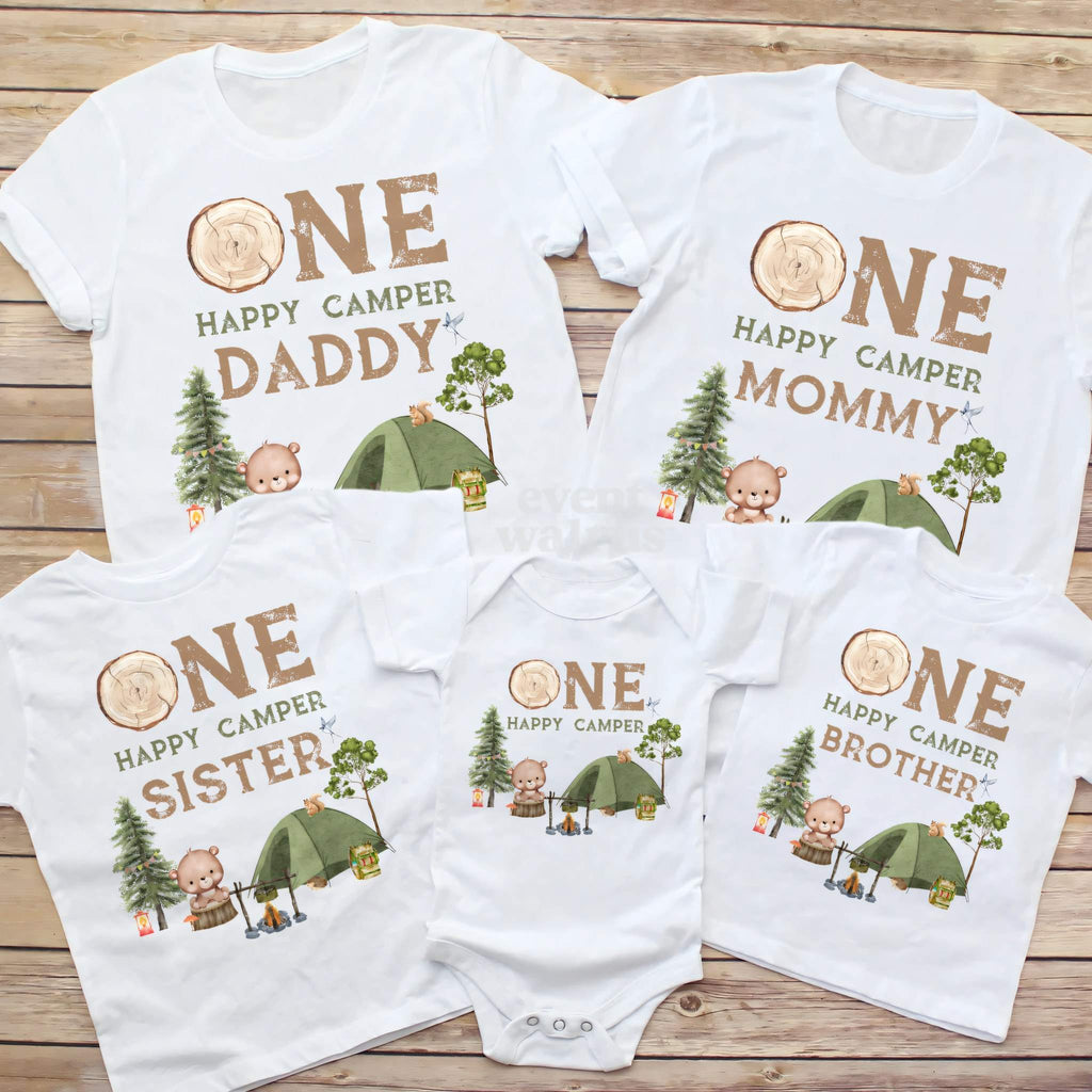 Daddy, Mommy, Sister, Brother and baby One Happy Camper shirts laid out on wood.