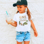 Girl in a ball cap holding a drink in a white One Happy Camper Friend shirt.