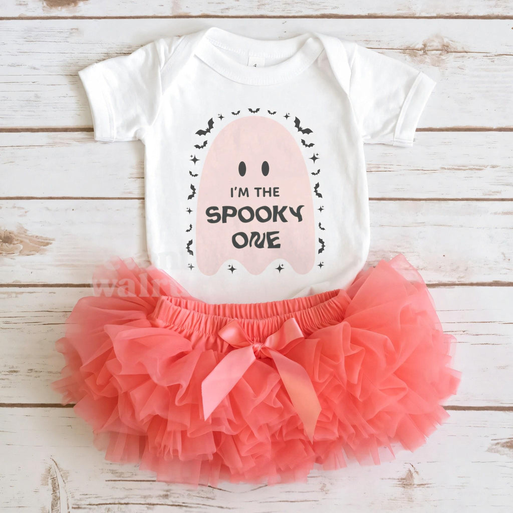 White Spooky One pink ghost bodysuit laid flat with a coral tutu on whitewashed wood.