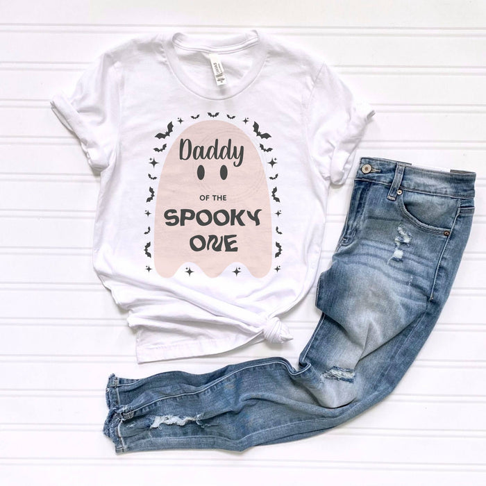 White Daddy of the Spooky One pink ghost tee laid flat beside jeans.