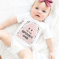 Baby girl with a pink bow lying in a white I'm the Spooky One pink ghost bodysuit.