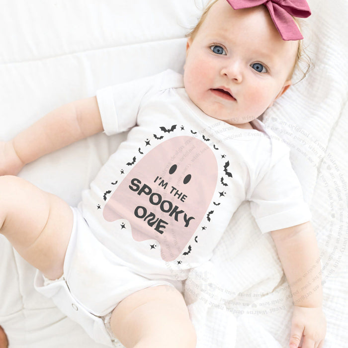 Baby girl with a pink bow lying in a white I'm the Spooky One pink ghost bodysuit.