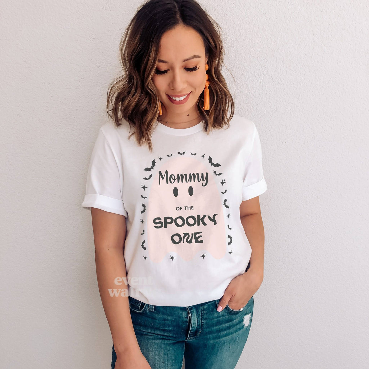Smiling woman in jeans wearing a white Mommy of the Spooky One shirt with a big pink ghost.