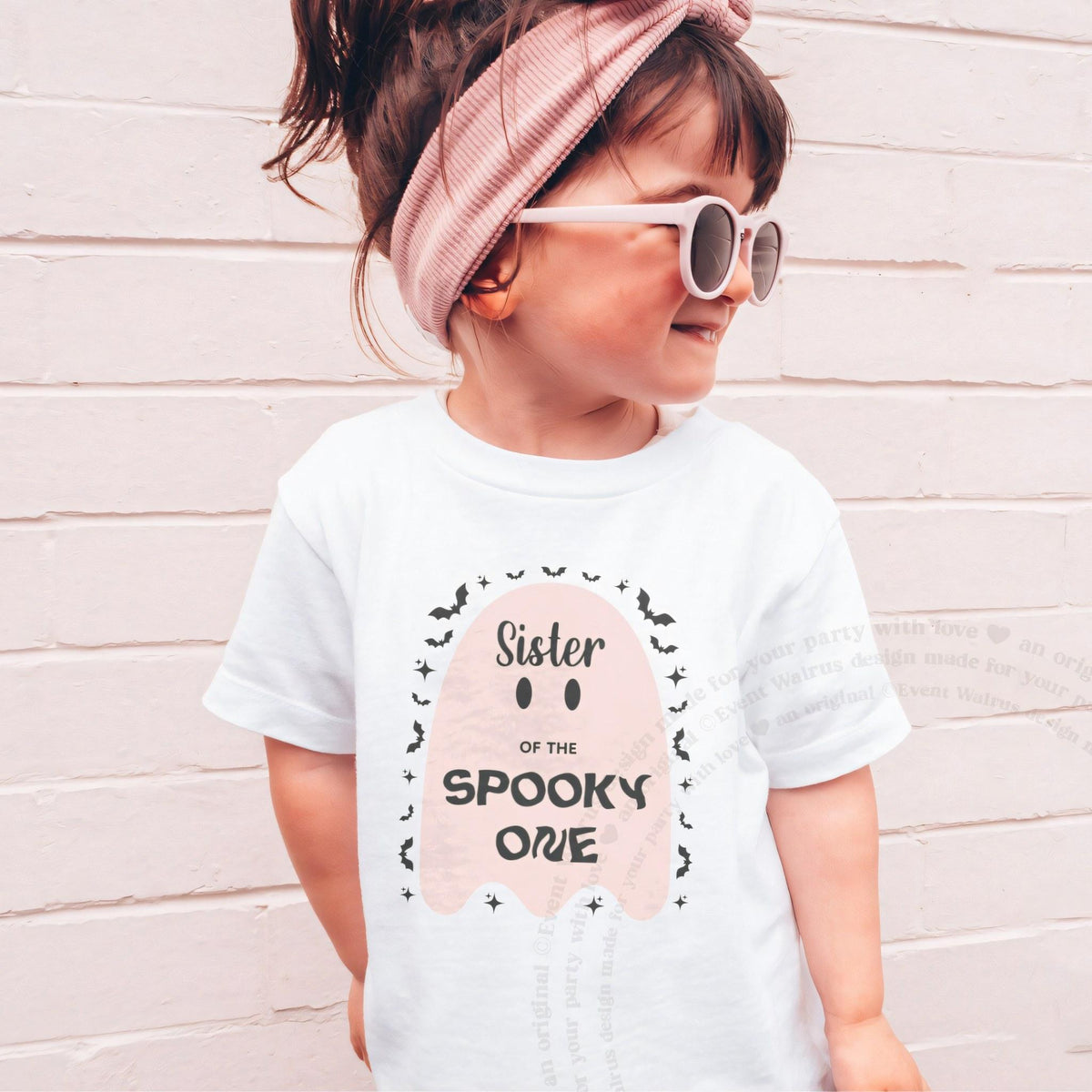 Girl in sunglasses and a pink headband wearing a white Sister of the Spooky One pink ghost shirt.