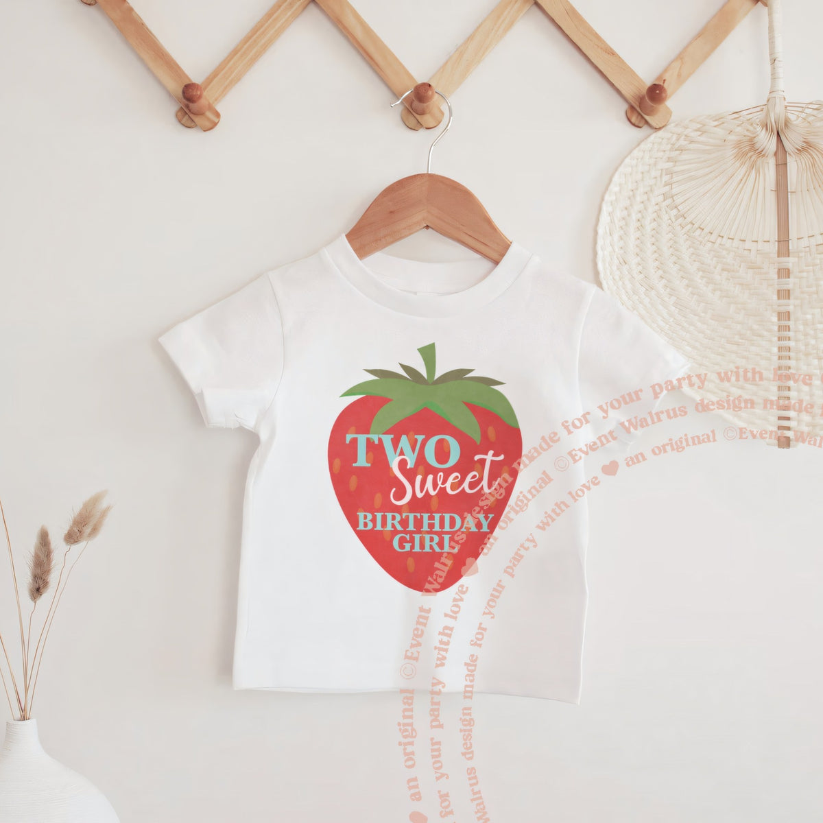 White big strawberry Two Sweet baby tee hanging on a wooden peg rail.