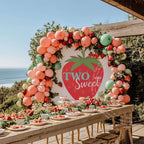 Big strawberry two sweet backdrop above a long seaside table with peach balloons.
