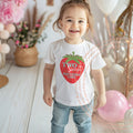 Smiling toddler girl at a pink party in a white Two Sweet Birthday Girl tee with a big strawberry.