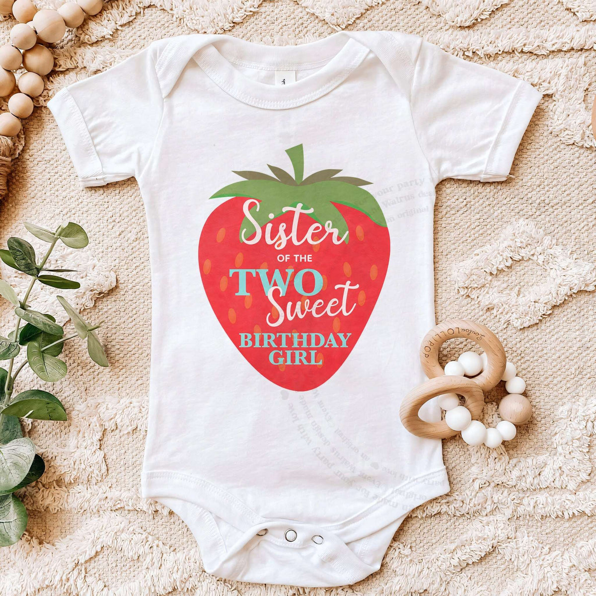 White Sister of the Two Sweet bodysuit on a beige blanket with a wooden teether.