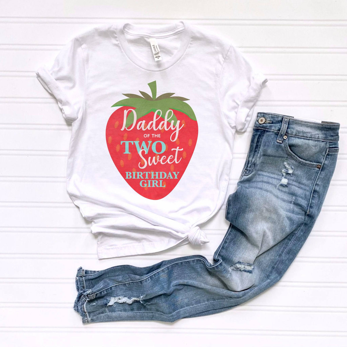 White Daddy of the Two Sweet tee laid flat beside jeans.