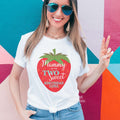 Smiling woman in sunglasses by a colorful wall wearing a white Two Sweet Mommy shirt with a big strawberry.