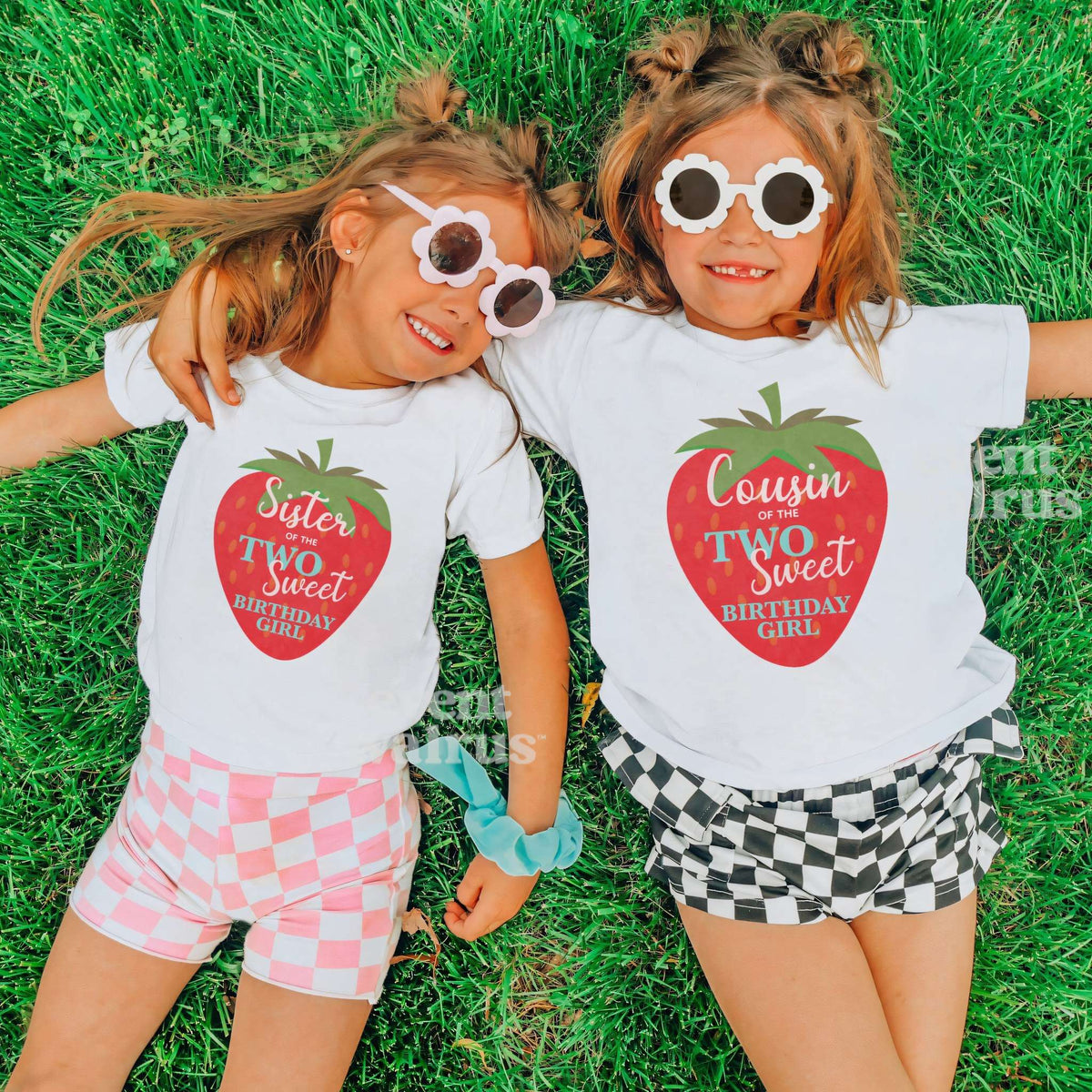 Two girls in heart sunglasses lying on grass in white Sister and Cousin big strawberry shirts.