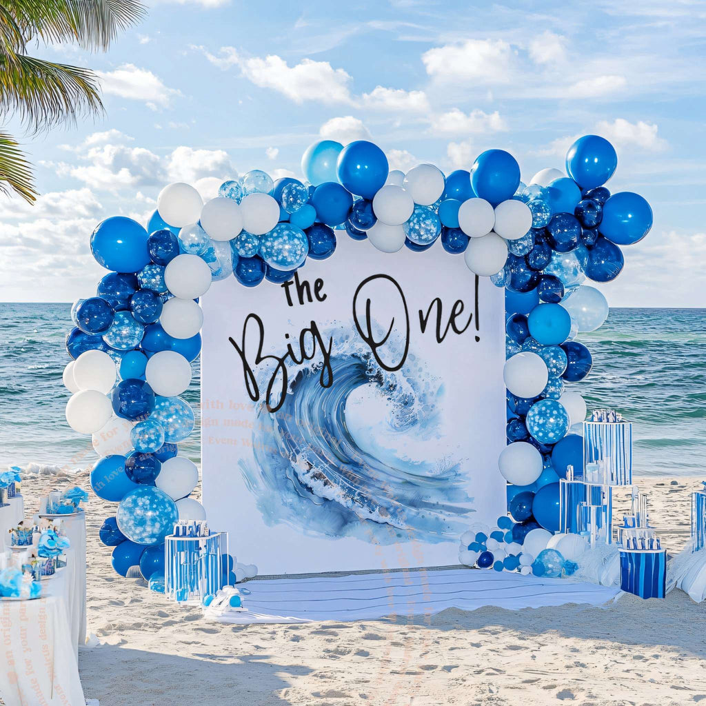 Watercolor wave the Big One backdrop on the sand with royal blue and white balloons.