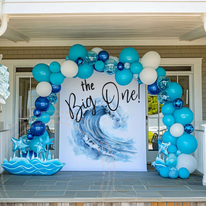Big Wave the Big One backdrop on a porch inside a blue and white balloon arch.
