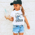 Girl in a ball cap wearing a white It's the Big One Sister wave tee.