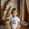 Little boy in a white It's the Big One Brother shirt with a blue wave.