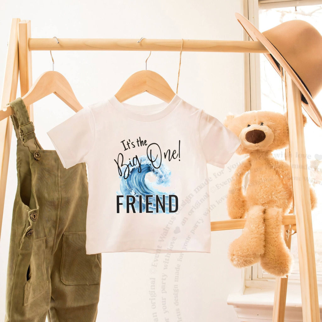 White toddler It's the Big One Friend shirt on a hanger beside a teddy bear.