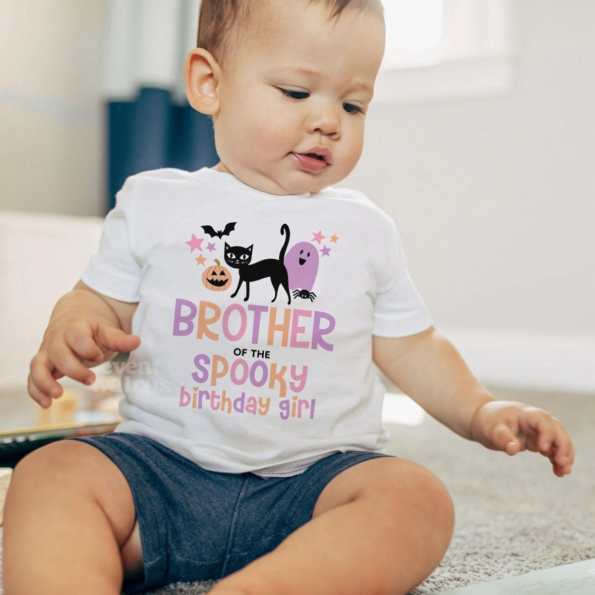 Baby boy sitting on a rug in a white Brother of the Spooky Birthday Girl baby tee.