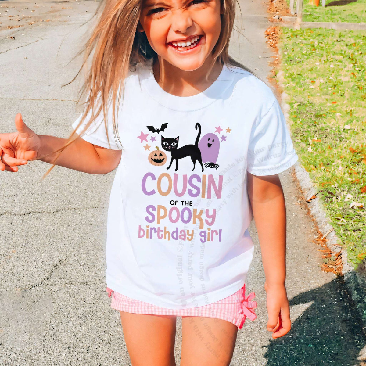 Laughing girl outdoors in a white Cousin of the Spooky Birthday Girl kids tee.