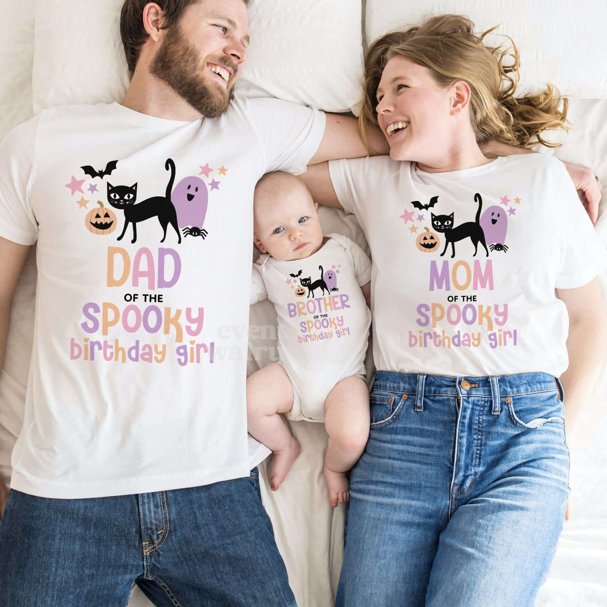 Dad and Mom lying beside their baby, all in white black cat Spooky Birthday Girl shirts.