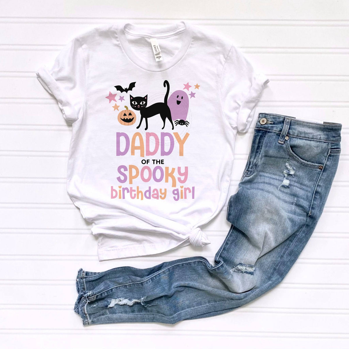 White Daddy of the Spooky Birthday Girl tee laid flat beside jeans.