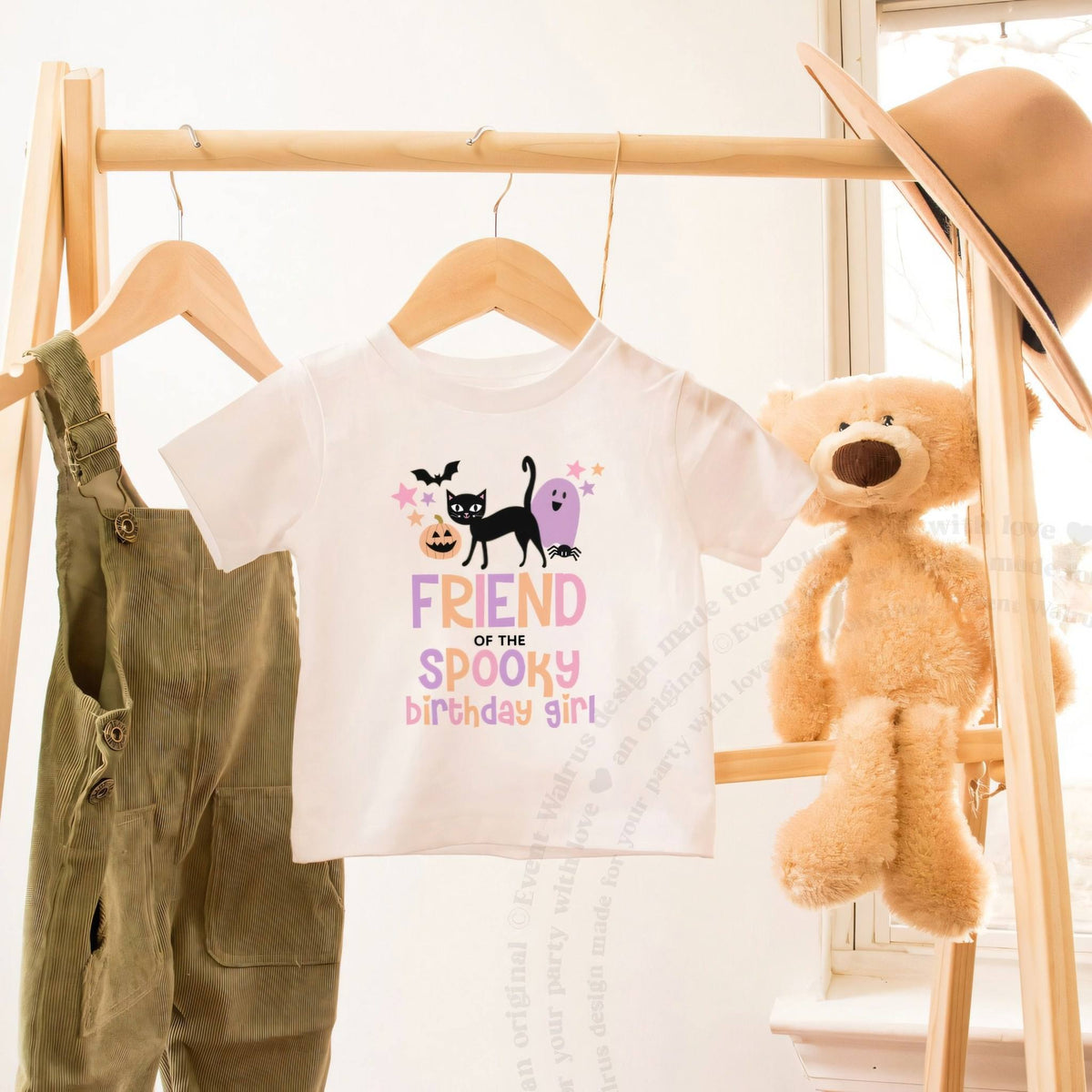 White Friend of the Spooky Birthday Girl toddler tee on a wooden clothes rack beside a teddy bear.
