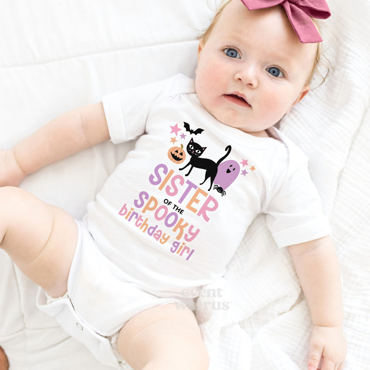 Baby girl with a pink bow lying in a white Sister of the Spooky Birthday Girl bodysuit.