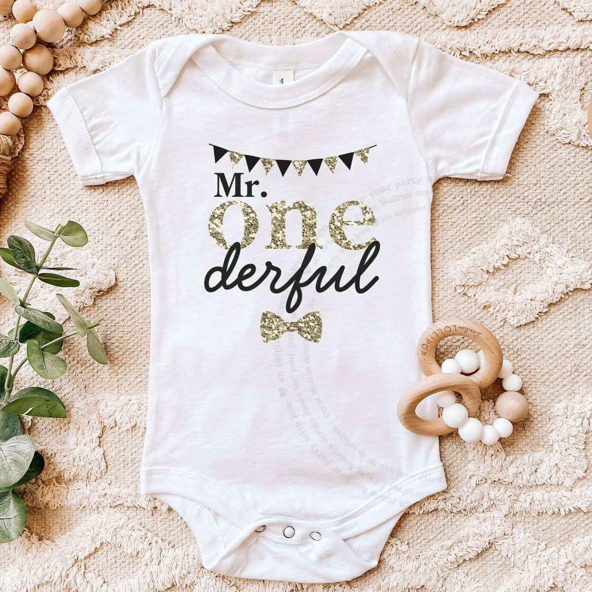 White Mr Onederful bodysuit on a beige blanket with a wooden teether.