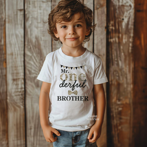 Little boy against a weathered wood wall in a white Mr Onederful Brother tee.