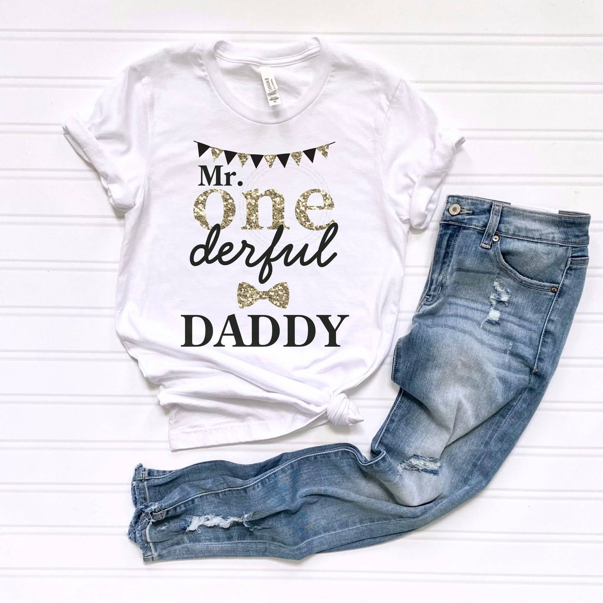 White Mr Onederful Daddy tee laid flat beside jeans.