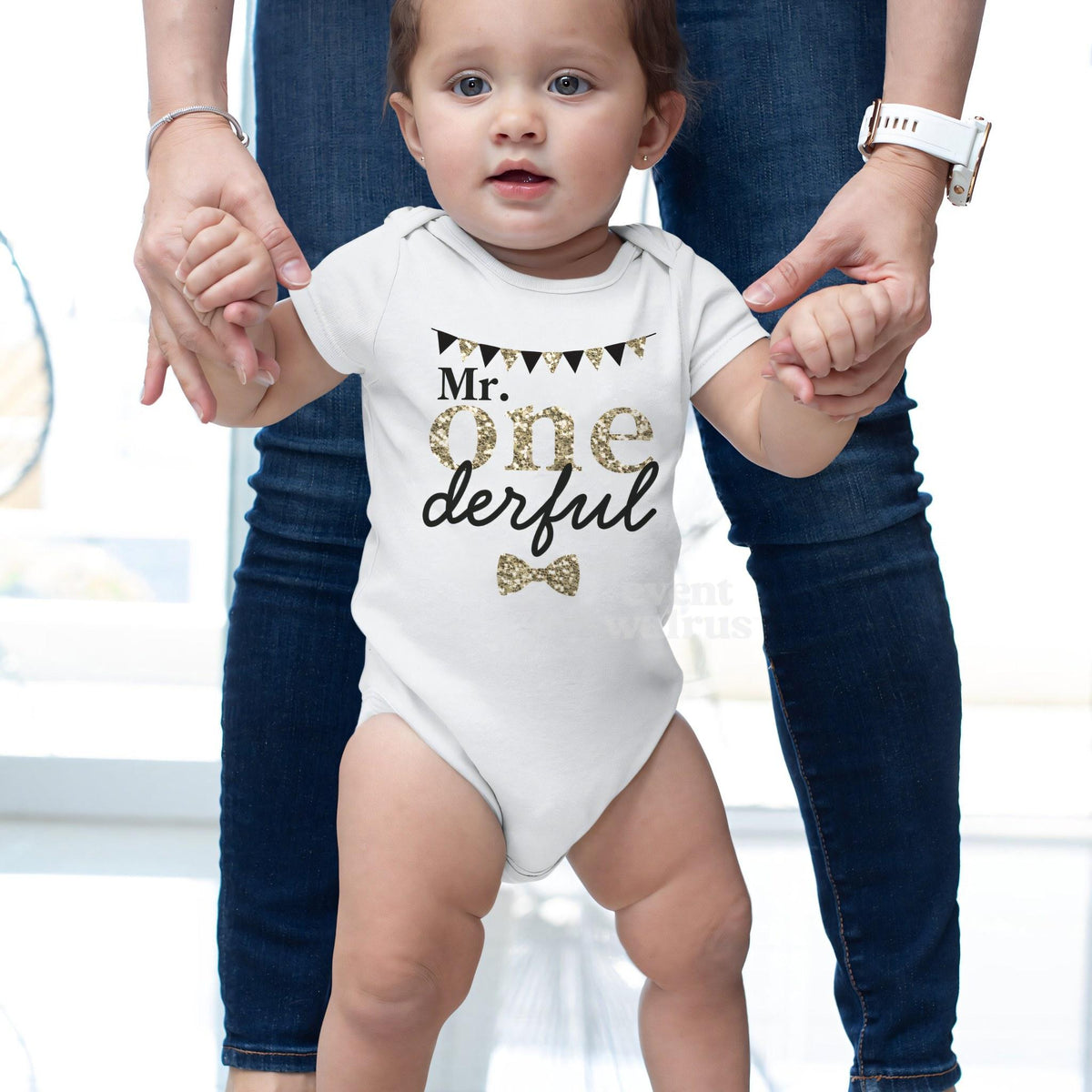 Baby taking steps while holding Mom's hands, in a white Mr Onederful bodysuit.